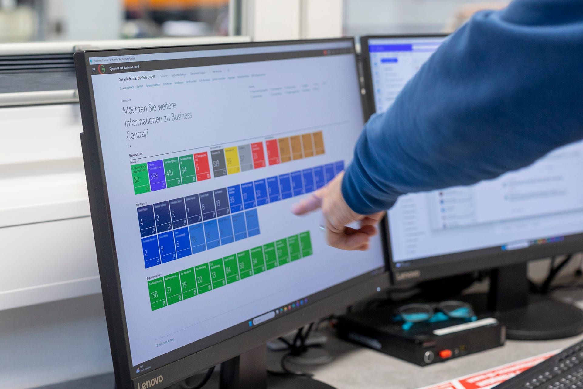 Business Central with coloured Cues tiles, a hand pointing at the screen
